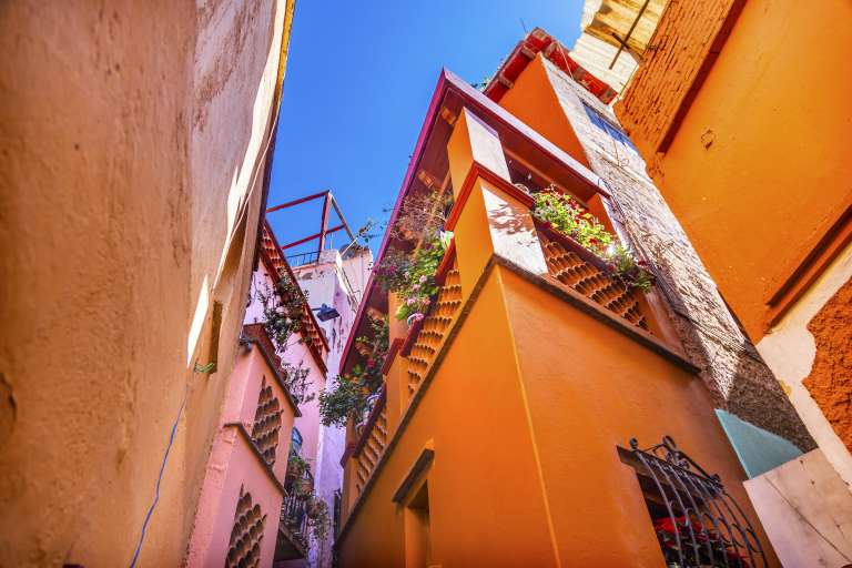 Callejón del beso en Guanajuato
El nombre de este lugar se debe a la leyenda de Carmen, hija sobreprotegida de un reputado señor, y Don Carlos, un joven minero de la zona.
Cuentan que se enamoraron a espaldas del padre y que este, al enterarse, encerró a su hija para siempre. Don Carlos, desesperado, vio que su balcón daba a un callejón muy estrecho, y que casi tocaba con la pared del edificio que tenía enfrente. Dedicó entonces todo su dinero a comprar la casa para así hablar con ella durante la noche. Hasta que el padre lo descubrió y asesinó a Carmen.
De esta triste historia procede el nombre del callejón, convertido ya, con sus 69 centímetros de ancho, en uno de los principales destinos turísticos de la zona junto con el célebre museo de las momias.