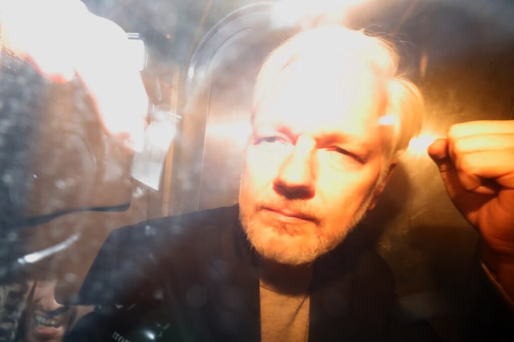 Julian Assange saluda a fotógrafos y periodistas mientras abandona en un vehículo policial, este miércoles, el tribunal de Southwark de Londres. / AFP