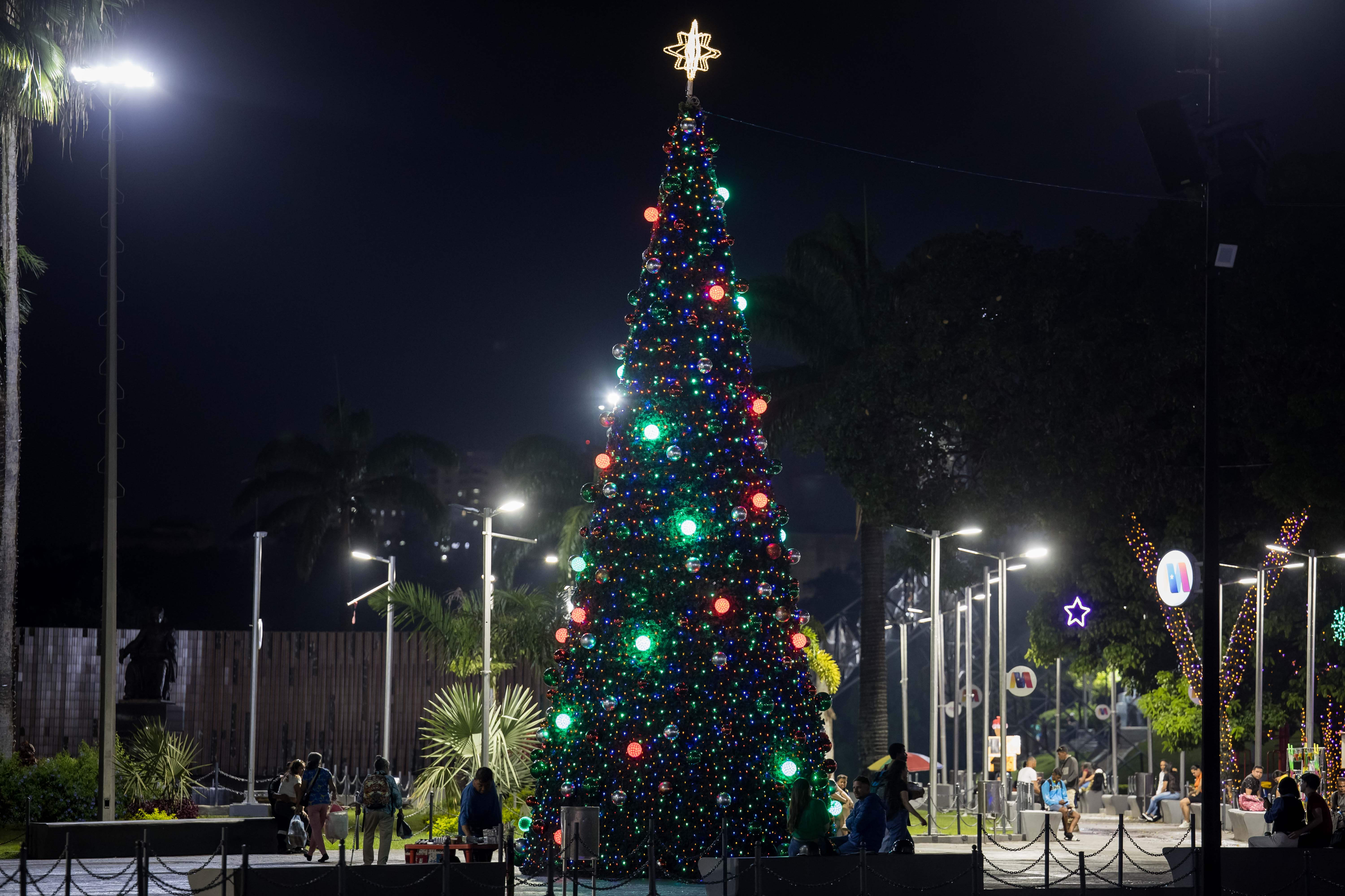 -FOTOGALERÍA- AME3906. CARACAS (VENEZUELA), 01/10/2024.- Personas caminan junto a un árbol navideño este lunes, en Caracas (Venezuela). En un mensaje televisado, el presidente de Venezuela, Nicolás Maduro, anunció el adelanto de las fiestas navideñas: “Y por eso este año, en homenaje a ustedes, en agradecimiento a ustedes, voy a decretar el adelanto de la Navidad para el 1 de octubre. Arranca la Navidad el 1 de octubre para todos y todas. Llegó la Navidad con paz, felicidad y seguridad” EFE/ Miguel Gutiérrez