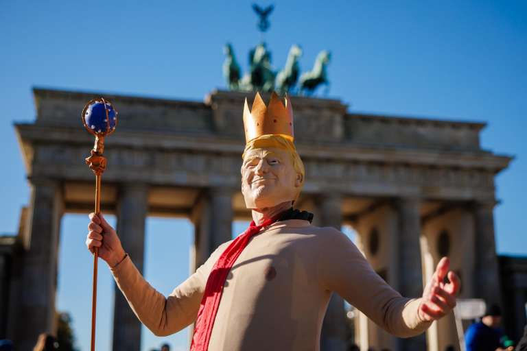 Una persona viste un disfraz del presidente estadounidense Donald J. Trump con una corona en la cabeza durante una manifestación frente a la Puerta de Brandeburgo en Berlín.