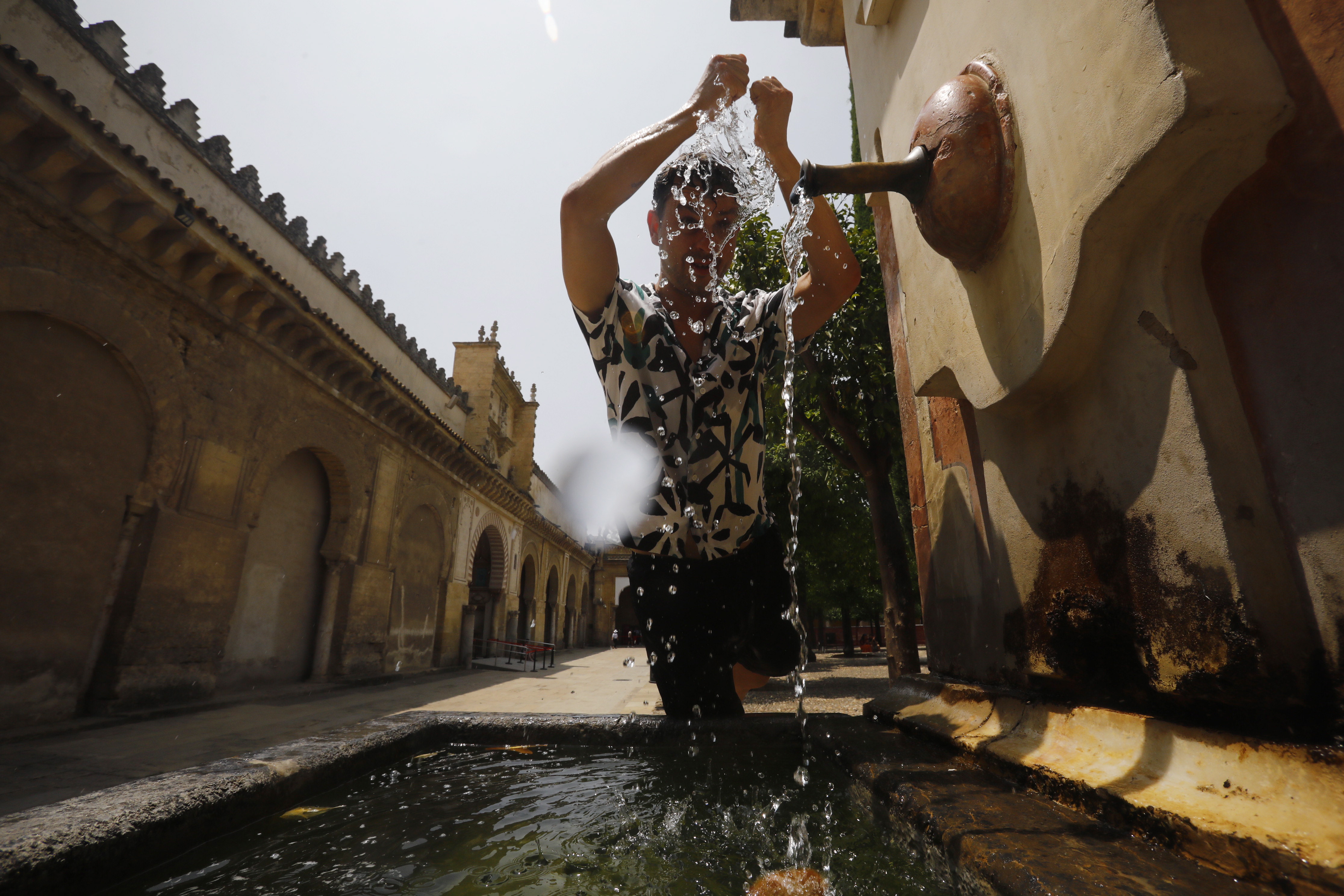 GRAFAND3272. CÓRDOBA, 28/06/2023.-Un joven se refresca en una fuente de del Patio de los Naranjos de la Mezquita-Catedral de Córdoba. La primera ola de calor que afecta a España este verano llega a su fin este miércoles con valores aún muy altos, hasta 42 grados, sobre todo en el centro y sur peninsular, aunque ya sin superar los umbrales establecidos para estos episodios de calor extremo. EFE/Salas