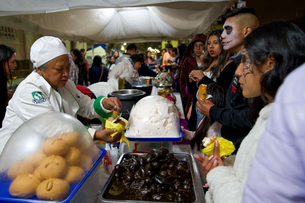 QUI01. QUITO (ECUADOR) 01/11/2024.- Personas disfrazadas consumen alimentos el pasado jueves en Quito (Ecuador). Las tradicionales 'guaguas' de pan, acompañadas de su inseparable colada morada, y personajes de las leyendas negras de Quito se dan cita este fin de semana en una nueva edición del festival 'Más allá de la vida', donde la capital ecuatoriana ensalza sus tradiciones en torno al Día de Difuntos. EFE/Vicente Costales