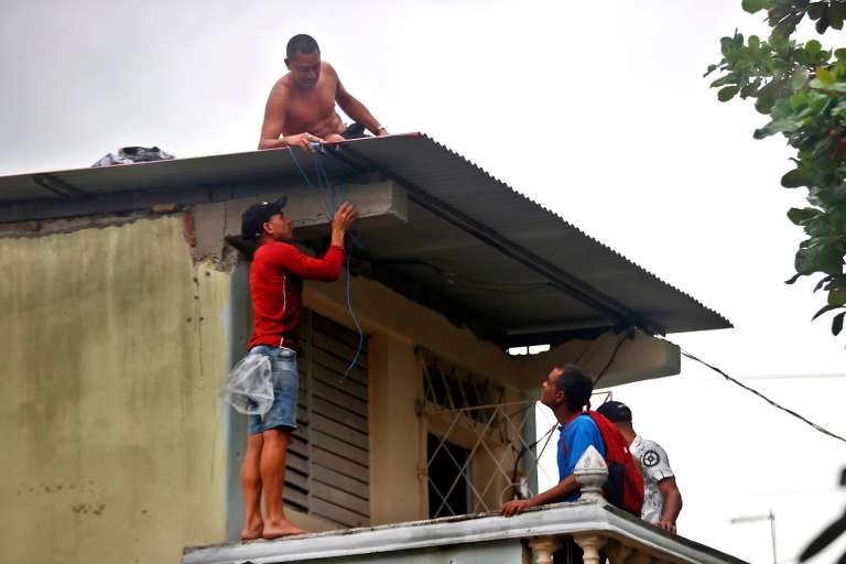 AME2711. SANTIAGO DE CUBA (CUBA), 28/10/2025.- Personas trabajan para asegurar el techo de una vivienda ante la posible llegada del huracán Melissa este martes, en Santiago de Cuba (Cuba). Tras su paso por la isla, se prevé que Melissa cruce el sureste de Cuba el miércoles y llegue a las Bahamas el jueves. EFE/ Ernesto Mastrascusa