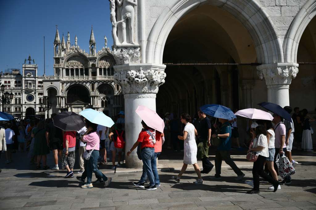 Tourists protect themselves from the sun with umbrellas at St Mark square, on a hot summer day in Venice on June 28, 2025.