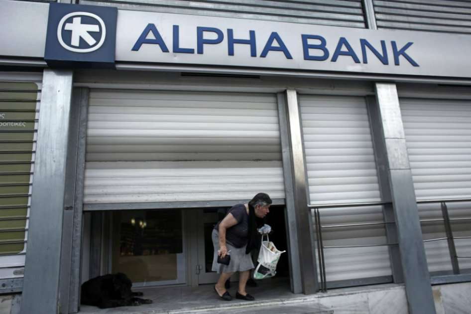 Un cliente saliendo por debajo de la persiana metálica de una sucursal bancaria de Alpha Bank AE cerrada en Atenas. / Bloomberg News