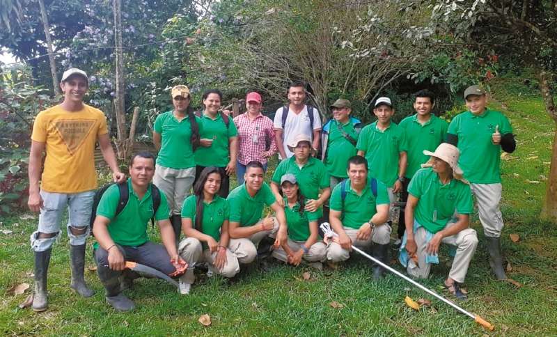 Hombres y mujeres jóvenes portan la camiseta de Comicacao y sonríen. Usan botas de campo y gorras.