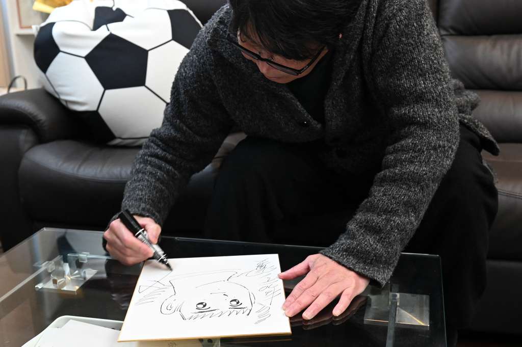 Esta foto tomada el 30 de enero de 2023 muestra al dibujante japonés y artista de manga Yoichi Takahashi, más conocido por su obra "Captain Tsubasa", añadiendo su autógrafo a un cuadro del personaje principal tras una entrevista con la AFP en su lugar de trabajo en Tokio.