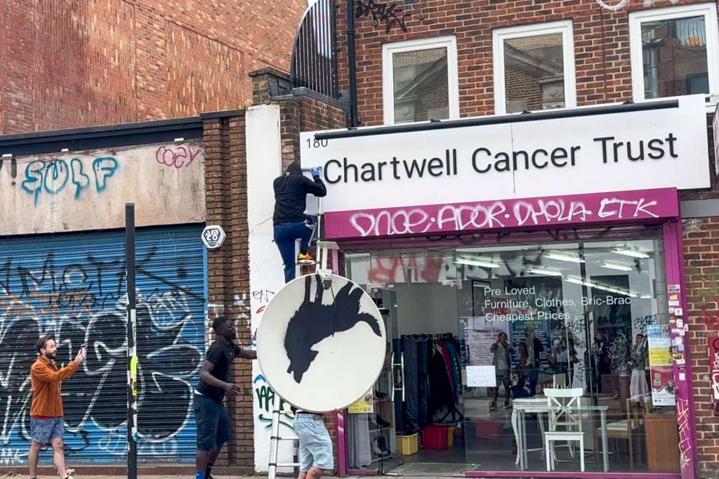 LONDRES, 08/08/2024.- Un grupo de encapuchados sube al tejado con una escalera y se lleva la creación del célebre artista urbano británico conocido como Banksy ante la mirada atónita de los viandantes en un barrio del sureste de Londres, la cuarta creación que desvela en lo que llevamos de semana. Antes, a través de una publicación en Instagram, el artista subió una doble fotografía -de noche y de día- del lugar escogido para su nueva creación, el tejado de un local del barrio de Peckham, al sureste de la capital británica, donde aparecía la silueta de un lobo dentro de una antena parabólica. EFE/Raúl Bobé