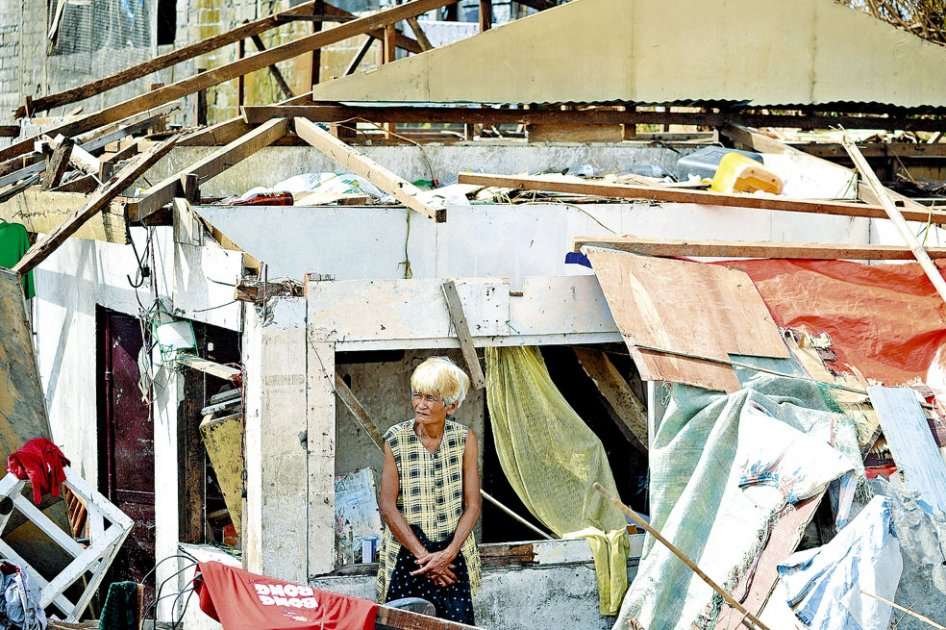 Una mujer espera al lado de su casa destruida en Tacloban, en la isla filipina de Leyte. / AFP