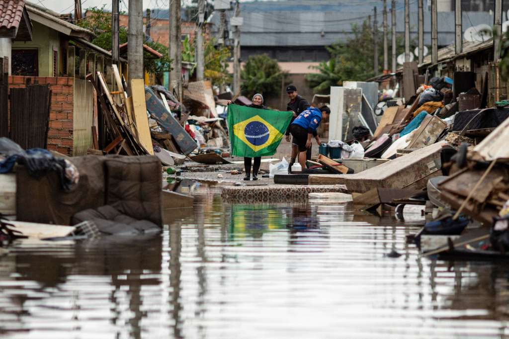 -FOTODELDÍA- AME1483. PORTO ALEGRE (BRASIL), 03/06/2024.- Una mujer sostiene una bandera de Brasil en medio de una calle afectada por las inundaciones, este lunes en Porto Alegre, Rio Grande do Sul (Brasil). Muchas ciudades siguen sufriendo por las inundaciones que azotaron el estado. Un mes después se reportan 172 muertos, 42 desaparecidos, 806 heridos y 616.600 personas se encuentran fuera de sus viviendas. EFE/ Daniel Marenco