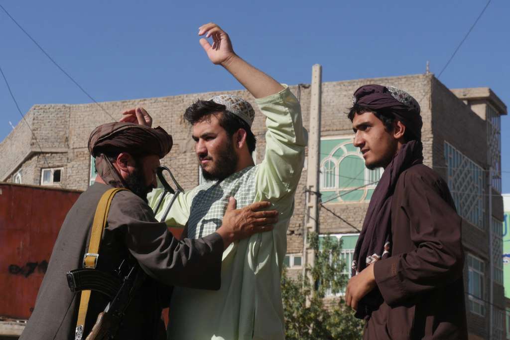 Un combatiente talibán (izquierda) cachea a los hombres en un puesto de control después de una explosión durante la oración del viernes en la mezquita de Gazargah, en Herat, el 2 de septiembre de 2022. -