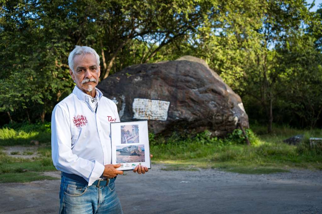 José Darío Nova, sobrino de Martha Vargas de Castro, frente a la gran roca de Armero. Sostiene un álbum fotográfico con imágenes antiguas del municipio.
