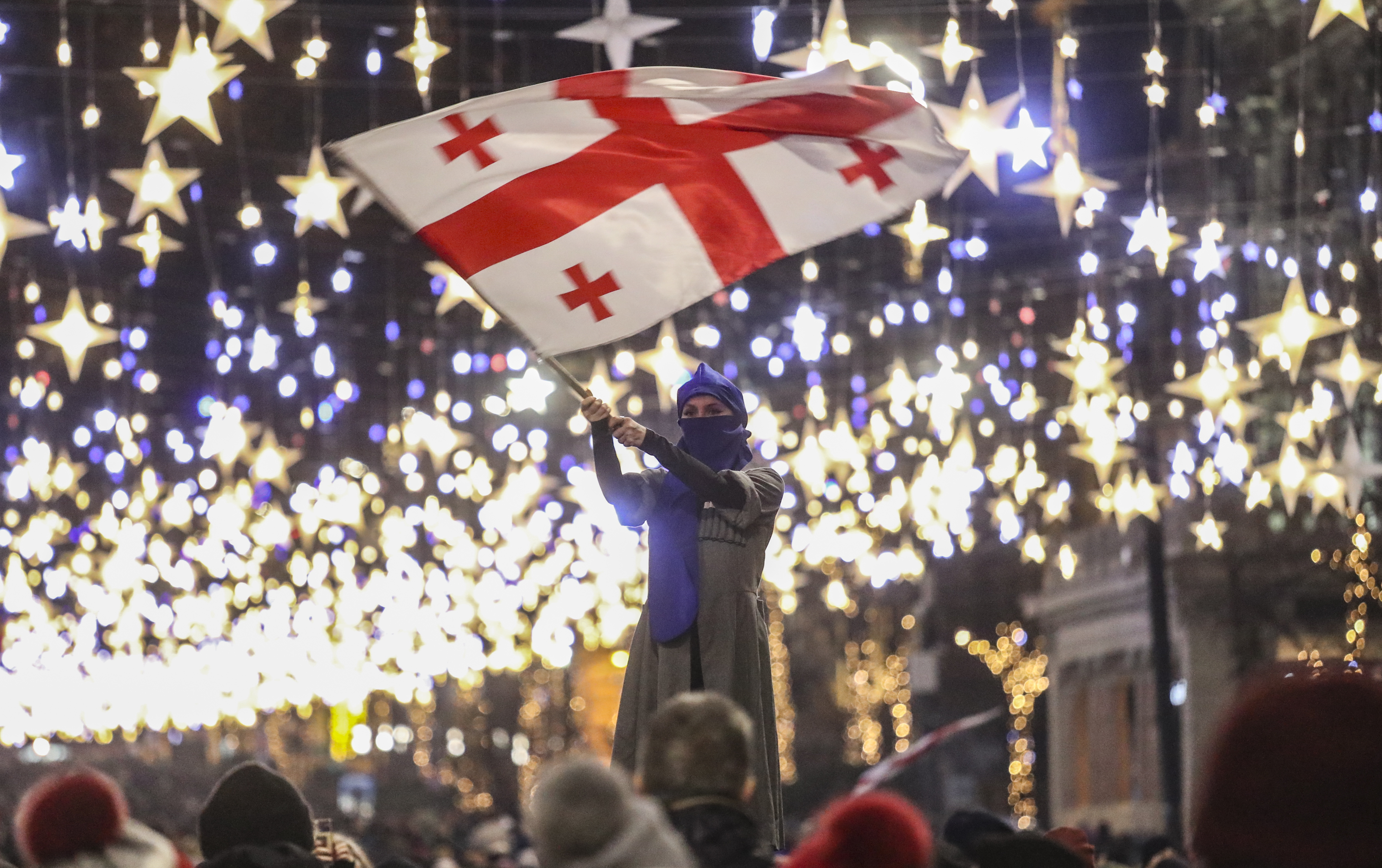 -FOTODELDÍA- EA7026. TBILISI (GEORGIA), 22/12/2024.- Una simpatizante de la oposición georgiana sostiene una bandera durante una protesta frente al Parlamento de Georgia este domingo, en Tiflis (Georgia). Los legisladores georgianos eligieron a Mikheil Kavelashvili como el nuevo presidente del país en una controvertida votación parlamentaria el 14 de diciembre, que desató acusaciones de ilegitimidad y protestas. La presidenta saliente de Georgia, Salome Zourabichvili, ha condenado el nombramiento de Kavelashvili como "ilegitimo" y se ha declarado a sí misma como la única representante legítima del poder en el país. EFE/EPA/DAVID MDZINARISHVILI