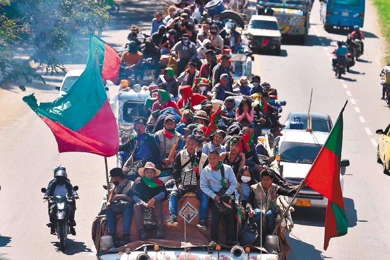 TOPSHOT - Colombian indigenous people taking part in a "Minga" (indigenous meeting) and heading to the city of Cali with the expectation of meeting President Ivan Duque, ride along the Pan-American highway in Jamundi, Colombia, on October 12, 2020. Thousands of indigenous people arrived in Cali where they hope to meet with President Duque, after having summoned him through a letter in recent days, in which they express concern about the increase of violence due to the presence of armed groups in their territories, the murder of indigenous and social leaders, and the recent massacres. / AFP / Luis ROBAYO