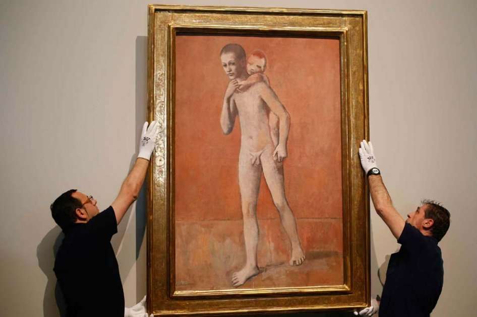 Dos operarios cuelgan el cuadro "Los dos Hermanos" (1905) de Pablo Picasso en la presentación de la Exposición del pintor malagueño en el Museo del Prado. / Efe