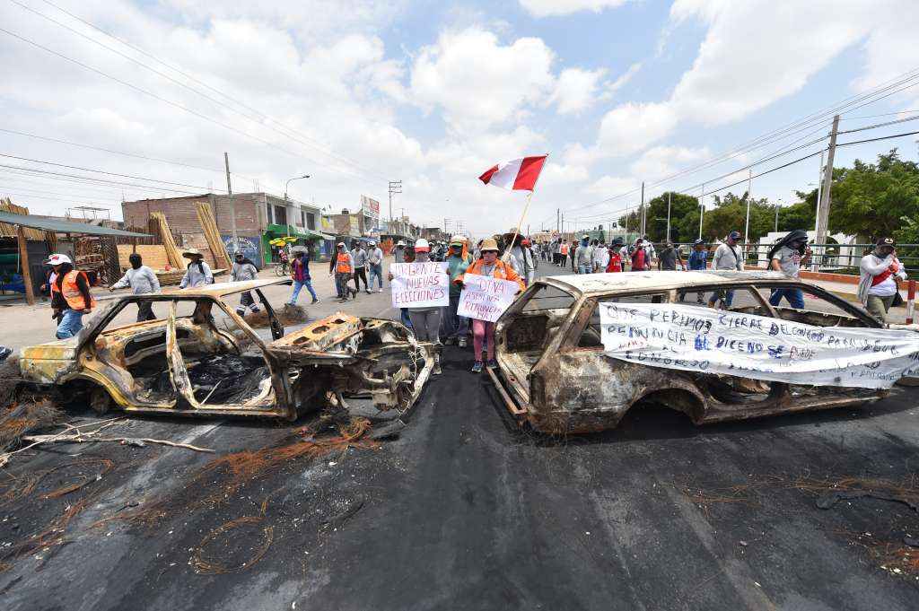 AME1035. AREQUIPA (PERÚ), 16/12/2022.- Simpatizantes de Pedro Castillo caminan entre dos vehículos incinerados mientras se manifiestan para pedir la salida de la presidenta Dina Boluarte y el cierre del Congreso hoy, en el distrito de la Joya, en Arequipa (Perú). Dieciocho personas han muerto desde que este domingo comenzaron las manifestaciones y protestas que exigen el adelanto de elecciones, la renuncia de la presidenta Dina Boluarte, el cierre del Congreso y la convocatoria a una asamblea constituyente. EFE/ José Sotomayor Jiménez