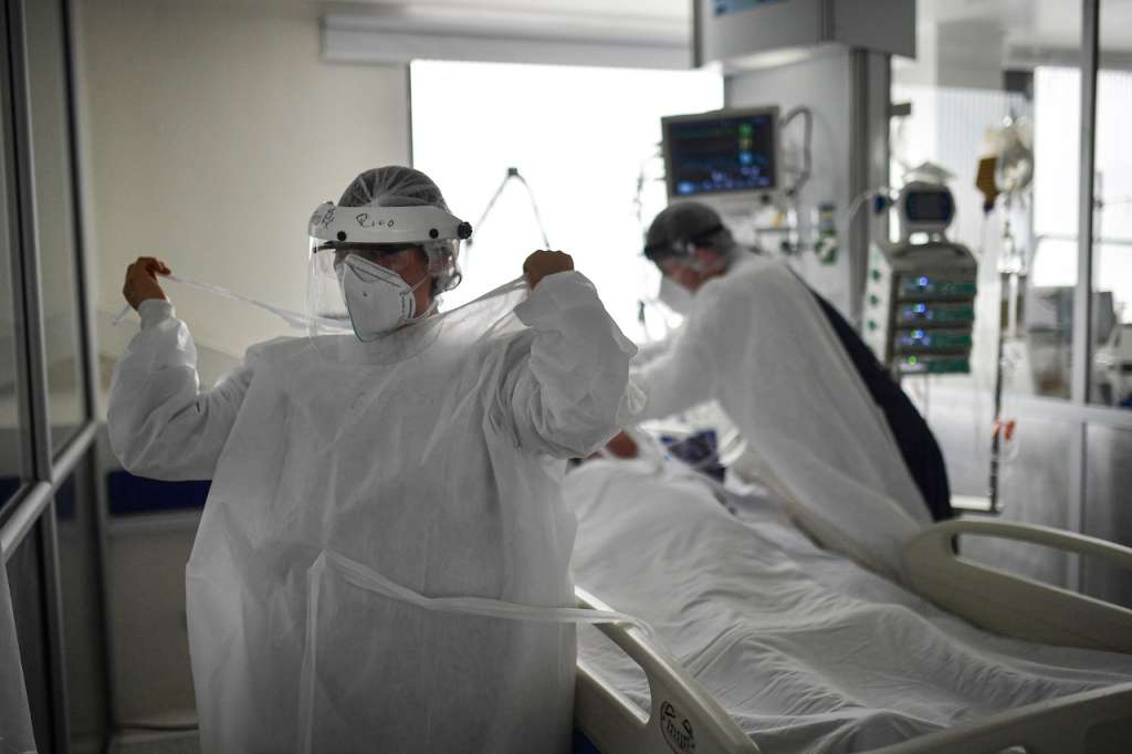 Un médico atiende un paciente al fondo, mientras otra médica se pone una bata