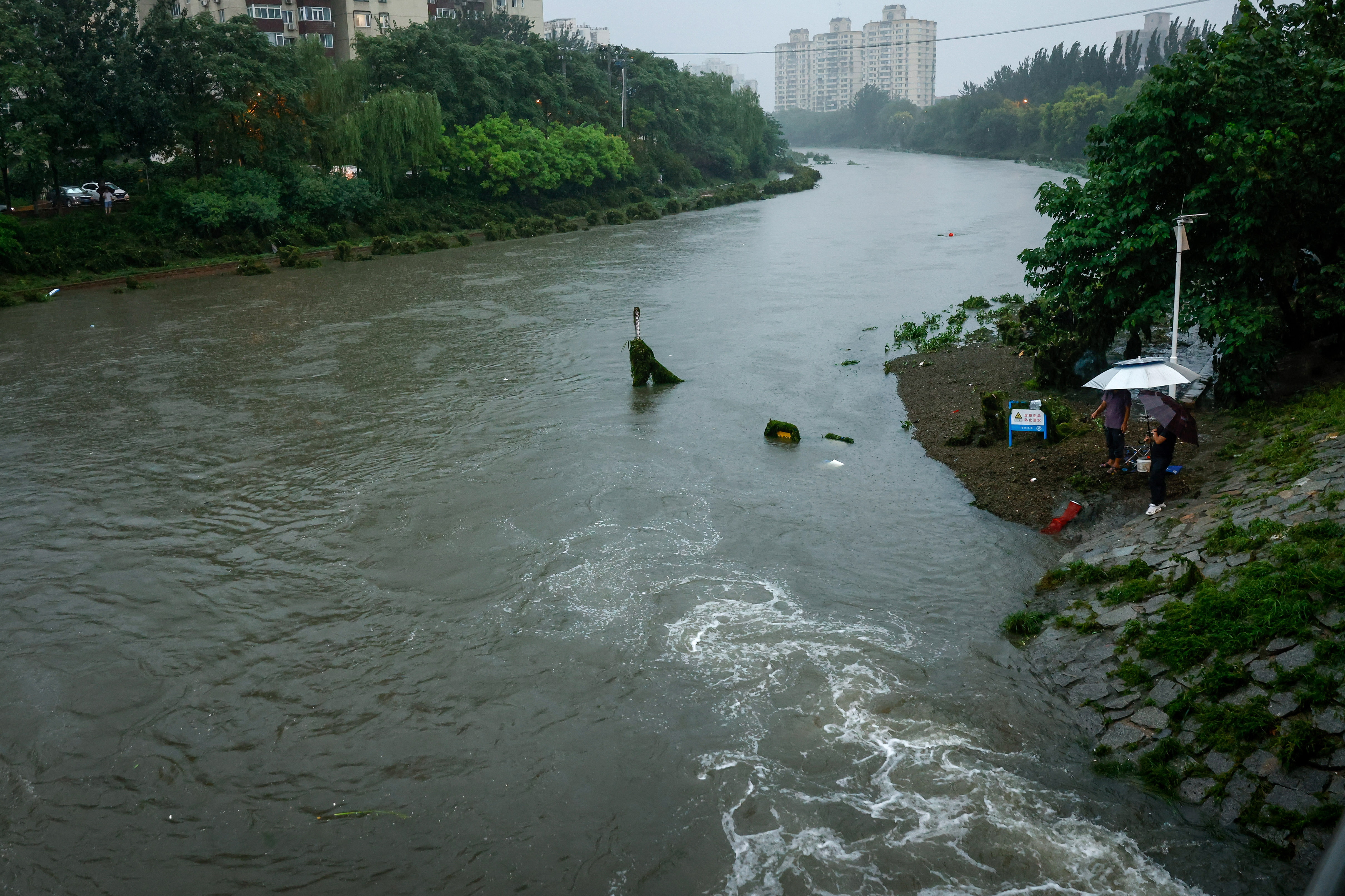 Beijing (China), 31/07/2023.- Men fish along a swollen river in Beijing, China, 31 July 2023. Beijing has recorded its heaviest rainfall this year as thousands have evacuated their homes from heavy rainfall brought by Typhoon Doksuri. EFE/EPA/MARK R. CRISTINO