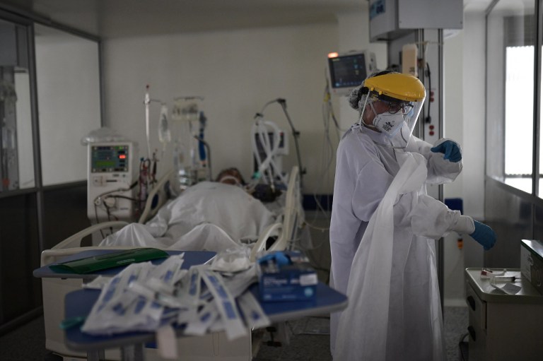 Una médica se pone una bata junto a un paciente intubado