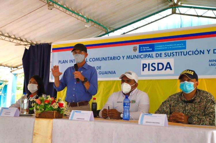 cuatro personas se encuentran en una mesa, una de ellas de pie, dando un discurso hacia el público