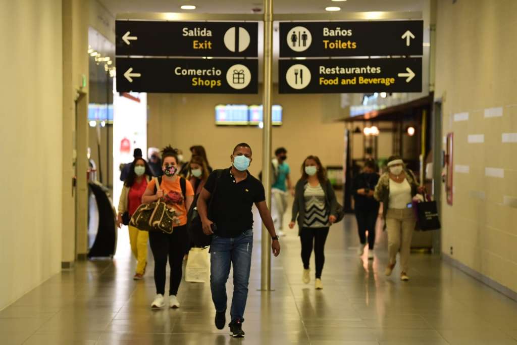Viajeros con tapabocas caminando por un pasillo del aeropuerto El Dorado, de Bogotá.