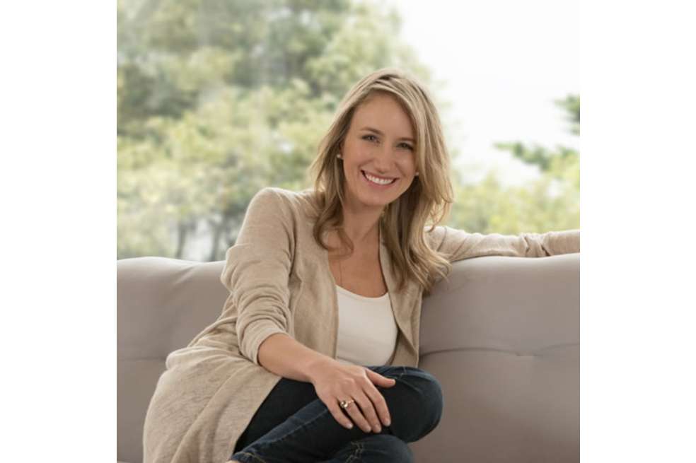 María Villegas está sentada en un sofá. Está vestida de colores claros, como beige y blanco.