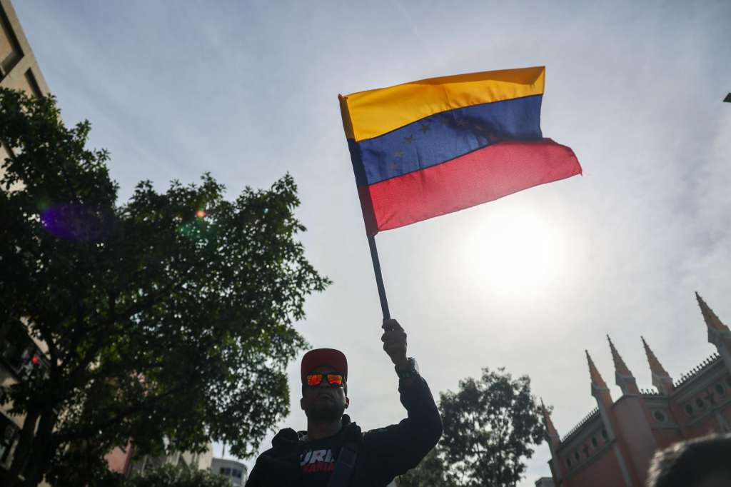 AME1591. CARACAS (VENEZUELA), 03/01/2026.- Un simpatizante del oficialismo sostiene una bandera de Venezuela este sábado en inmediaciones del Palacio de Miraflores en Caracas (Venezuela). Chavistas salieron a las calles del centro de Caracas para exigir que "devuelvan" al mandatario venezolano, Nicolás Maduro, luego de que el líder estadounidense, Donald Trump, anunciara la captura del gobernante suramericano en medio de un ataque con misiles durante la madrugada de hoy contra la capital venezolana y otras zonas del país. EFE/ Miguel Gutiérrez