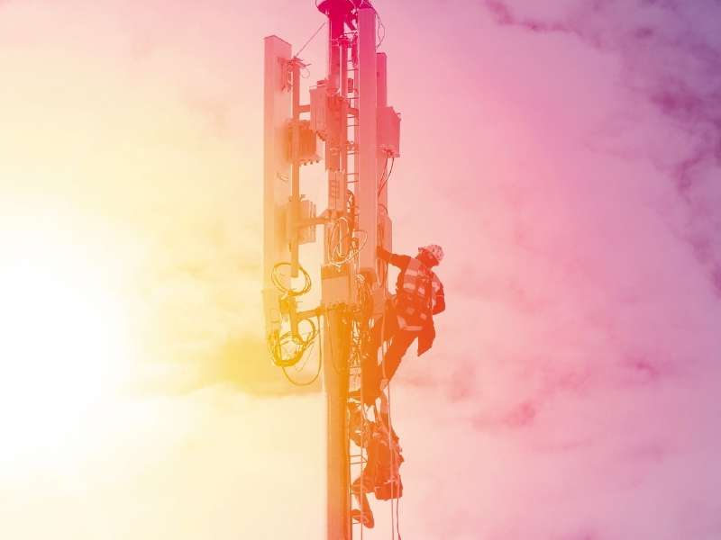 Technician working on communication tower on sunset blue sky