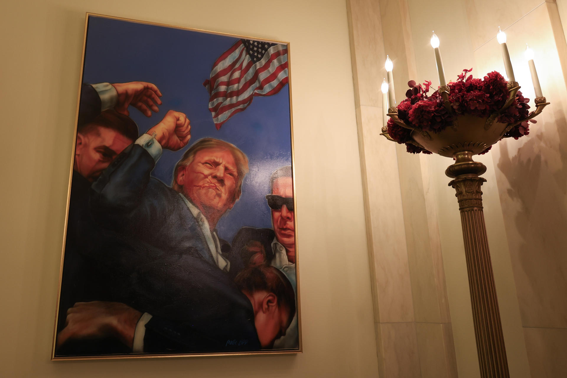 AME4625. WASHINGTON (ESTADOS UNIDOS), 01/12/2025.- Fotografía que muestra un cuadro que recrea el momento en que Donald Trump sobrevivió a un intento de asesinato el año pasado, este lunes, en la Casa Blanca, en Washington (Estados Unidos). Se trata de una pintura que muestra a Trump con el puño en alto y el rostro ensangrentado, escoltado por agentes del Servicio Secreto, en alusión a la imagen captada segundos después del atentado durante un mitin en Butler (Pensilvania) en julio de 2024. EFE/ Octavio Guzmán
