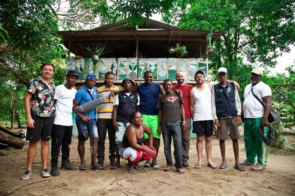 Parte del equipo de realizadores y tutores del colectivo en la casa de Andrés; pintor, músico y uno de los tres personajes principales de uno de los cortometrajes.La lucha no la están dando solos. Dentro del proyecto “Postales del Futuro”, los jóvenes de En Puja realizan un intercambio con el colectivo Puerto Creativo de Buenaventura. Se trata de un diálogo entre dos territorios atravesados por la noción de un puerto. Henry cuenta que incluso dentro de su colectivo había quienes apoyaban el proyecto pero que luego de escuchar de primera mano a los bonaverenses sobre lo que ha significado ese puerto para su ciudad, se convirtieron en sus opositores. “Ellos nos contaron, por ejemplo, que allá había agua solamente tres veces al día por unas horas determinadas. Si eso es así en una ciudad grande como esa, qué le espera a Nuquí que además también tiene ese tipo de dificultades”, dice.