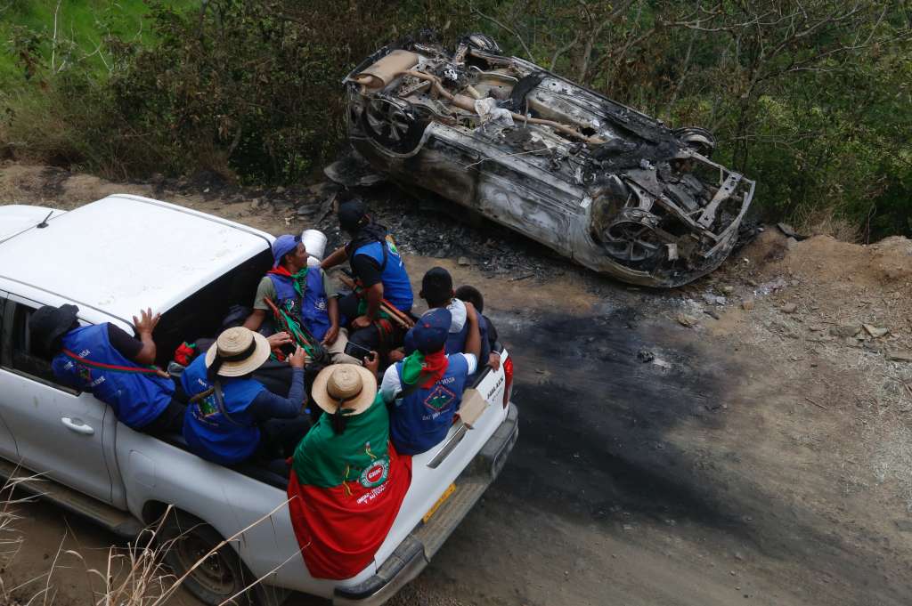 TORIBÍO (COLOMBIA), 19/03/2024.- Guardias indígenas pasan junto a un carro destruido en el que presuntamente se transportaban miembros del Estado Mayor Central (EMC), la mayor disidencia de las FARC, este martes en la vereda La Bodega de Toribío, departamento de Cauca (Colombia). Los indígenas de la zona realizan la velación de la lideresa nasa Carmelina Yule Paví, asesinada el pasado fin de semana cuando intentaba impedir que miembros de la columna Dagoberto Ramos del EMC se llevaran a un menor de edad indígena. EFE/ Ernesto Guzmán