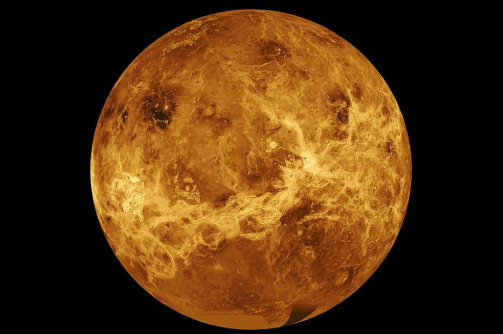 Imagen compuesta de Venus desde el espacio. El planeta es un globo moteado de color dorado y naranja oscuro sobre un fondo negro. A lo largo del tercio inferior, una línea ondulante dorada más clara cruza desde la parte inferior izquierda a lo largo del centro derecho. En la parte superior del planeta aparecen manchas más oscuras.