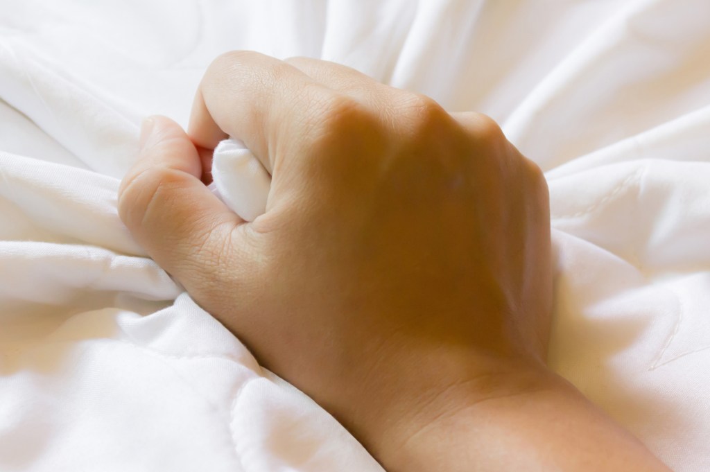 Hand grasp white bed sheet for good dreamy feeling in bed