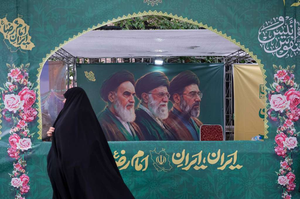 TEHERÁN, 29/04/2026.- Una mujer vestida con el tradicional chador pasa delante de un cartel en Teherán que muestra a los tres líderes supremos de la República Islámica, incluido el actual Mojtaba Jameneí. Miles de iraníes participaron este miércoles en marchas de lealtad al líder supremo, Mojtaba Jameneí, a quien no se ha visto en público desde su nombramiento y en medio de los mensajes de Estados Unidos de que hay dudas acerca de quién lidera la República Islámica. EFE/Jaime León