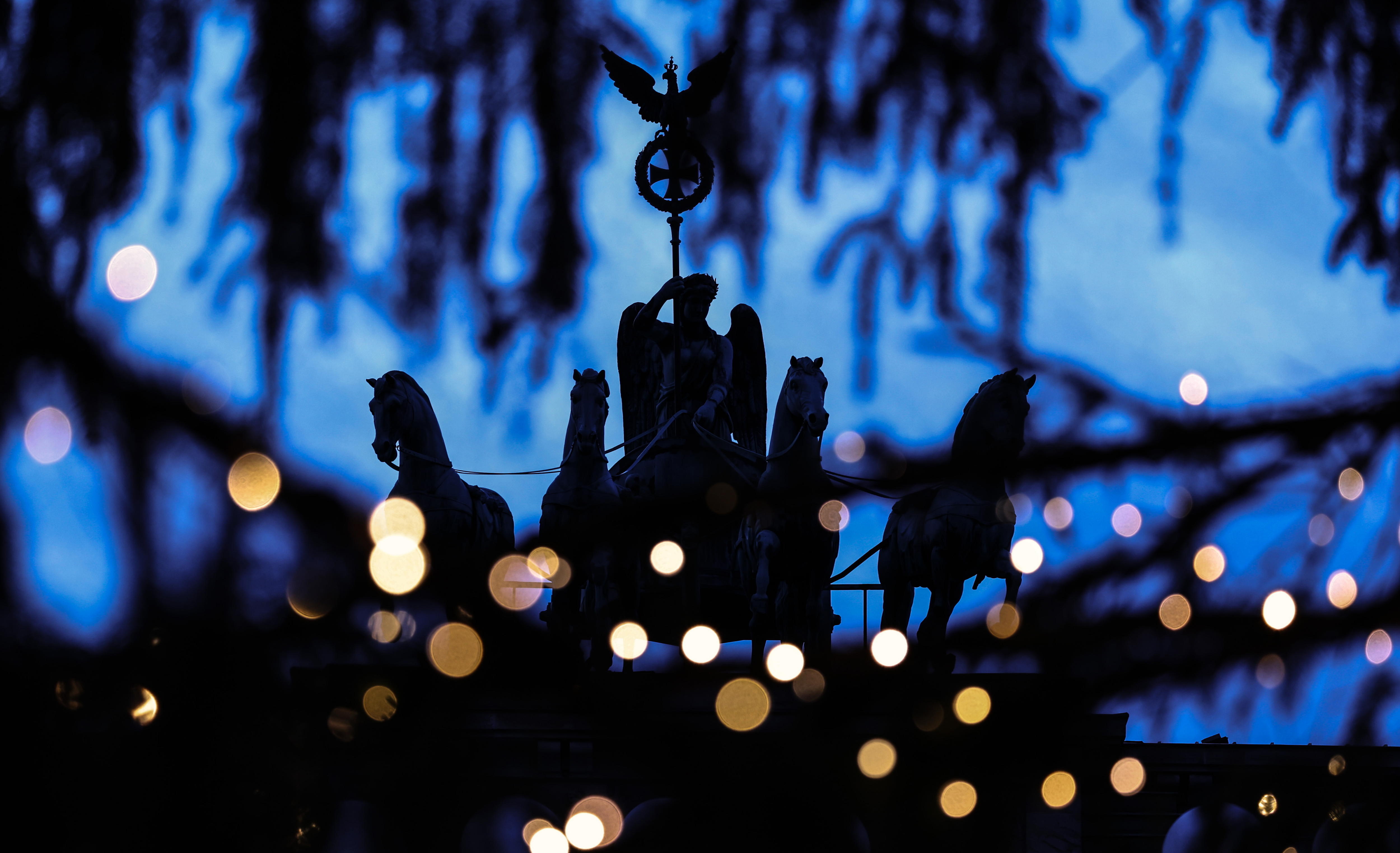 -FOTODELDÍA- BERLÍN (ALEMANIA), 24/12/2024.- Vista de la estatua de la Cuadriga de la Puerta de Brandemburgo entre luces borrosas colocadas sobre un árbol de Navidad, este martes en Berlín (Alemania). EFE/ Filip Singer