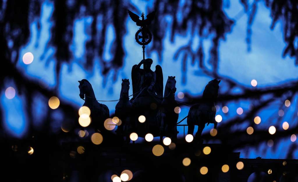 -FOTODELDÍA- BERLÍN (ALEMANIA), 24/12/2024.- Vista de la estatua de la Cuadriga de la Puerta de Brandemburgo entre luces borrosas colocadas sobre un árbol de Navidad, este martes en Berlín (Alemania). EFE/ Filip Singer