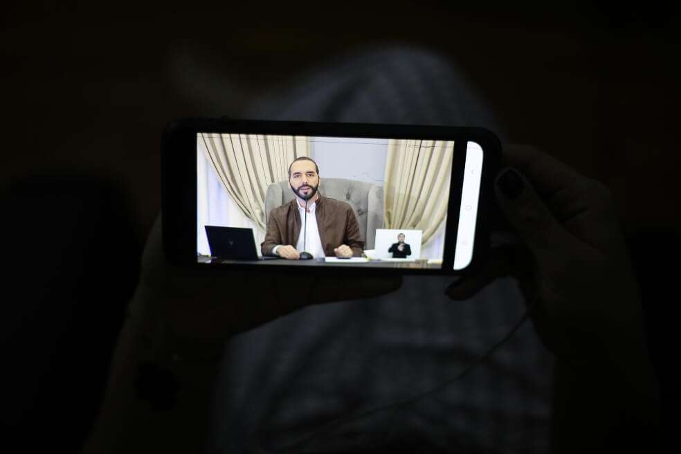 Una joven sintoniza desde su teléfono móvil la cadena de televisión donde el presidente de El Salvador, Nayib Bukele, cuenta los avances en la lucha contra el coronavirus. / EFE
