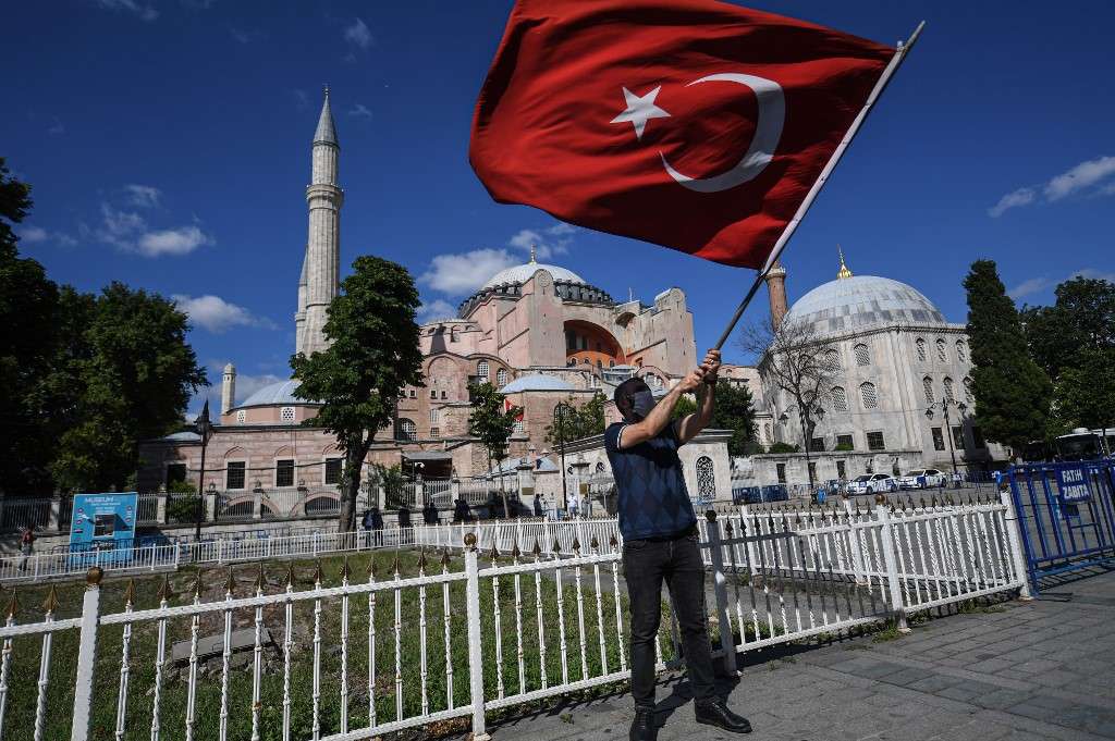 A man waves a Turkish national flag as people gather outside the Hagia Sophia museum on July 10, 2020 in Istanbul to celebrate after a top Turkish court revoked the sixth-century Hagia Sophia's status as a museum, clearing the way for it to be turned back into a mosque. - The Council of State, the country's highest administrative court which on July 2 debated a case brought by a Turkish NGO, cancelled a 1934 cabinet decision and ruled the UNESCO World Heritage site would be reopened to Muslim worshipping. The sixth-century Istanbul building -- a magnet for tourists -- has been a museum since 1935, open to believers of all faiths thanks to a cabinet decision stamped by modern Turkey's founder Mustafa Kemal Ataturk. (Photo by Ozan KOSE / AFP)