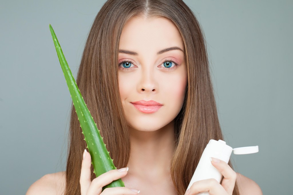Beautiful Spa Model Woman with Healthy Skin, Green Aloe Leaf, Long Hair and Moisturizer Tube