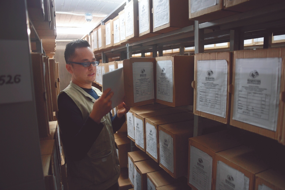 Un hombre está revisando unas cajas donde hay archivos de inteligencia.