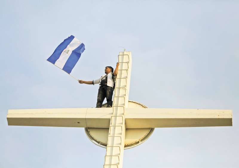 Un católico nicaragüense ondea una bandera del país en la punta de la Catedral Metropolitana de Managua. / AFP