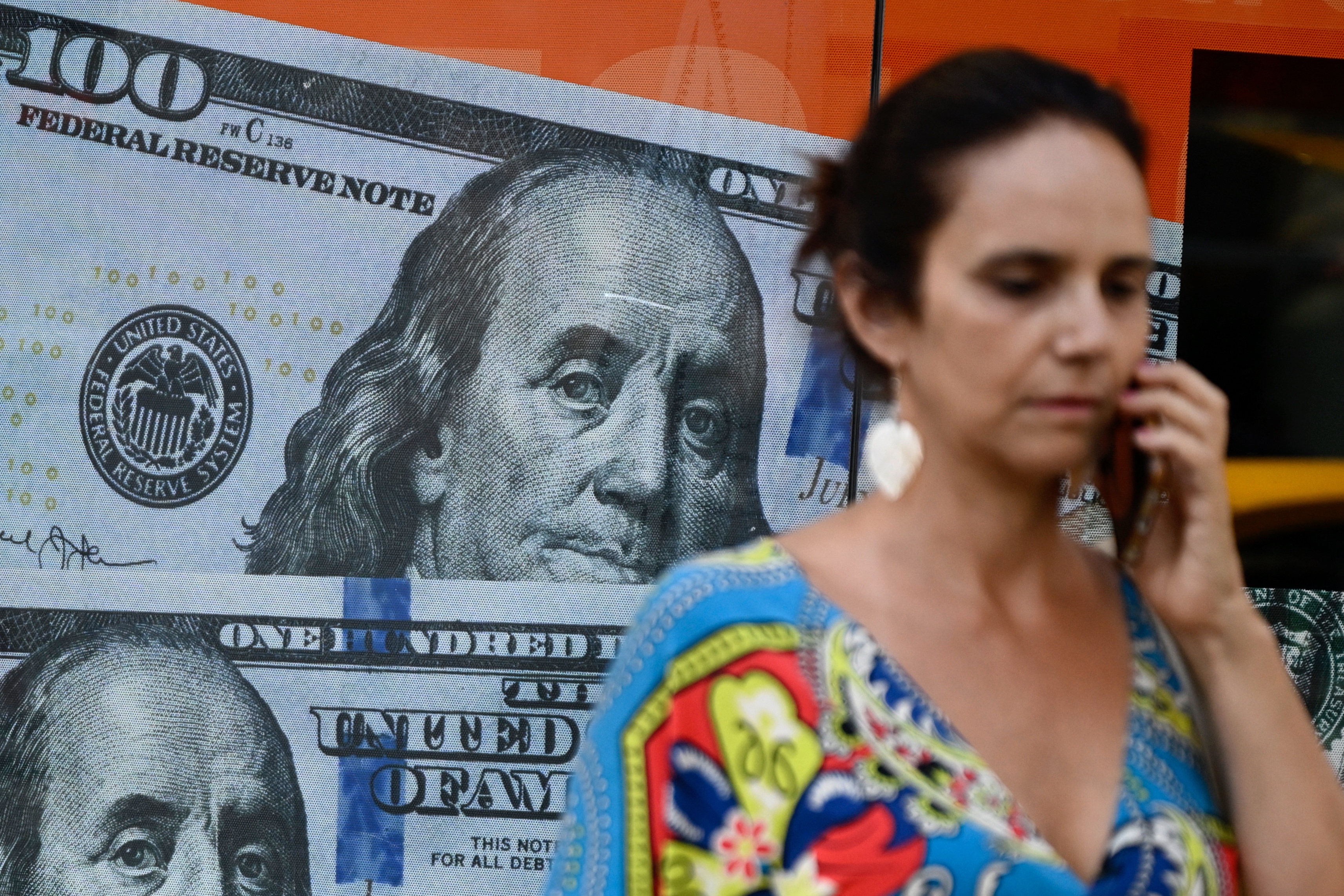 (FILES) A woman walks past an image of one hundred US dollar notes in Buenos Aires on December 12, 2023.