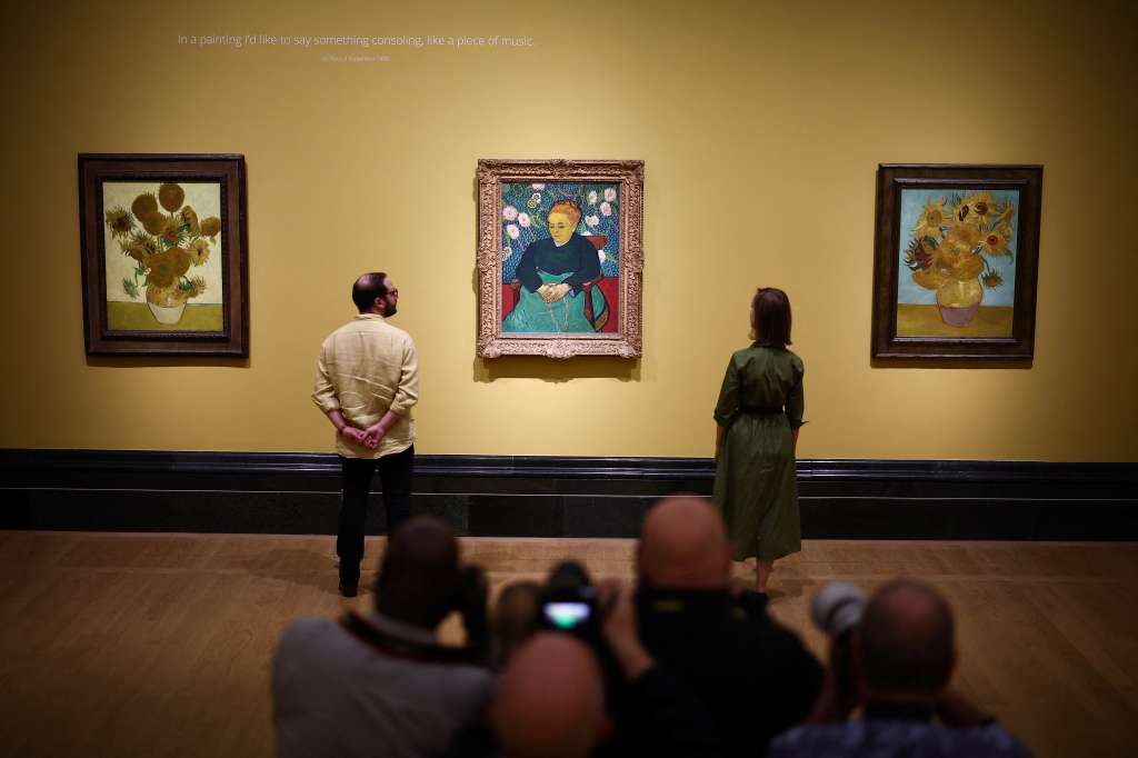 TOPSHOT - Visitors look at (from L) three paintings made by late Dutch artist Vincent Van Gogh "Sunflowers" 1888, "Lullaby : Madame Augustine Roulin Rocking a Cradle" 1889 and "Sunflowers" 1889, during a press preview for "Van Gogh: Poets and Lovers" exhibition at the National Gallery, in London, on September 9, 2024. (Photo by HENRY NICHOLLS / AFP) / RESTRICTED TO EDITORIAL USE - MANDATORY MENTION OF THE ARTIST UPON PUBLICATION - TO ILLUSTRATE THE EVENT AS SPECIFIED IN THE CAPTION