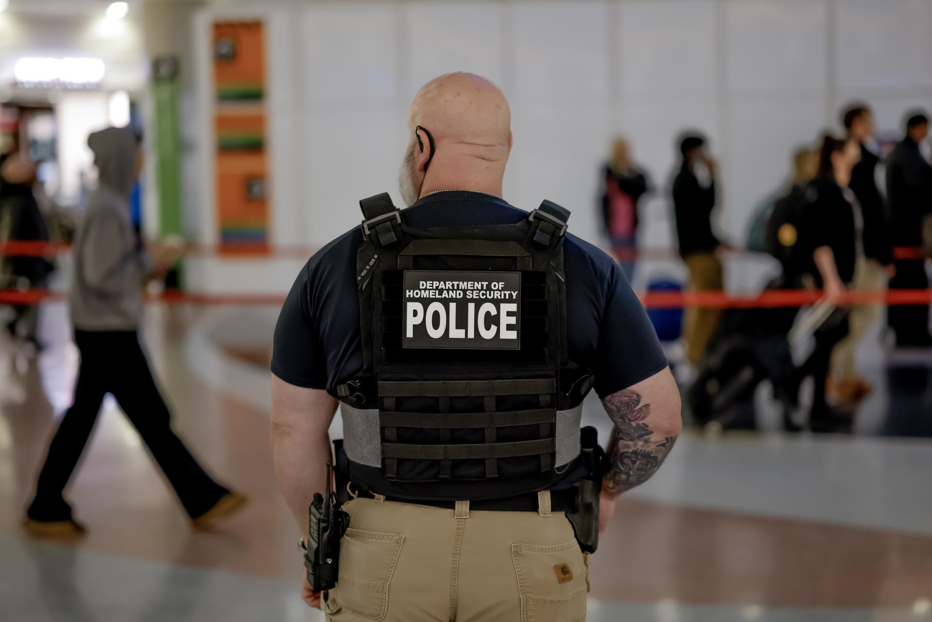 ATLANTA (United States), 19/03/2026.- A Department of Homeland Security federal police officer stands watch as air passengers wait in long security screening lines to pass through a Transportation Security Administration (TSA) checkpoint at Hartsfield–Jackson Atlanta International Airport in Atlanta, Georgia, USA, 19 March 2026. The ongoing partial US government shutdown has impacted air travel, leading to widespread security checkpoint delays.TSA screeners, along with thousands of other federal employees within the Department of Homeland Security (DHS), are working without pay until the funding lapse is resolved. EFE/EPA/ERIK S. LESSER