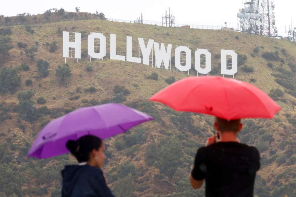 EA7247. BOGOTÁ (COLOMBIA), 06/05/2025.- Fotografía de archivo fechada el 20 de agosto de 2023 que muestra personas observando el letrero de Hollywood bajo la lluvia cerca del parque Lake Hollywood en Los Ángeles, California (EE.UU.). La amenaza de un arancel del 100 % a las películas producidas en el extranjero sacude los cimientos de Hollywood, una industria que lleva décadas tratando de mantenerse a flote ante el éxodo de colosos del entretenimiento, deudas millonarias y pérdida de atractivo. EFE/EPA/Caroline Brehman /ARCHIVO