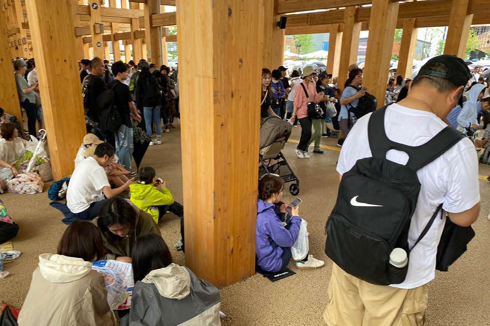 Visitantes a la Exposición Universal de Osaka 2025 sentados en el suelo del Gran Aro de madera que rodea los pabellones.