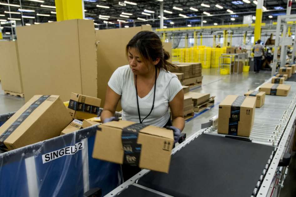 Un empleado de Amazon.com levanta una caja desde un transportador al centro de cumplimiento de la compañía.