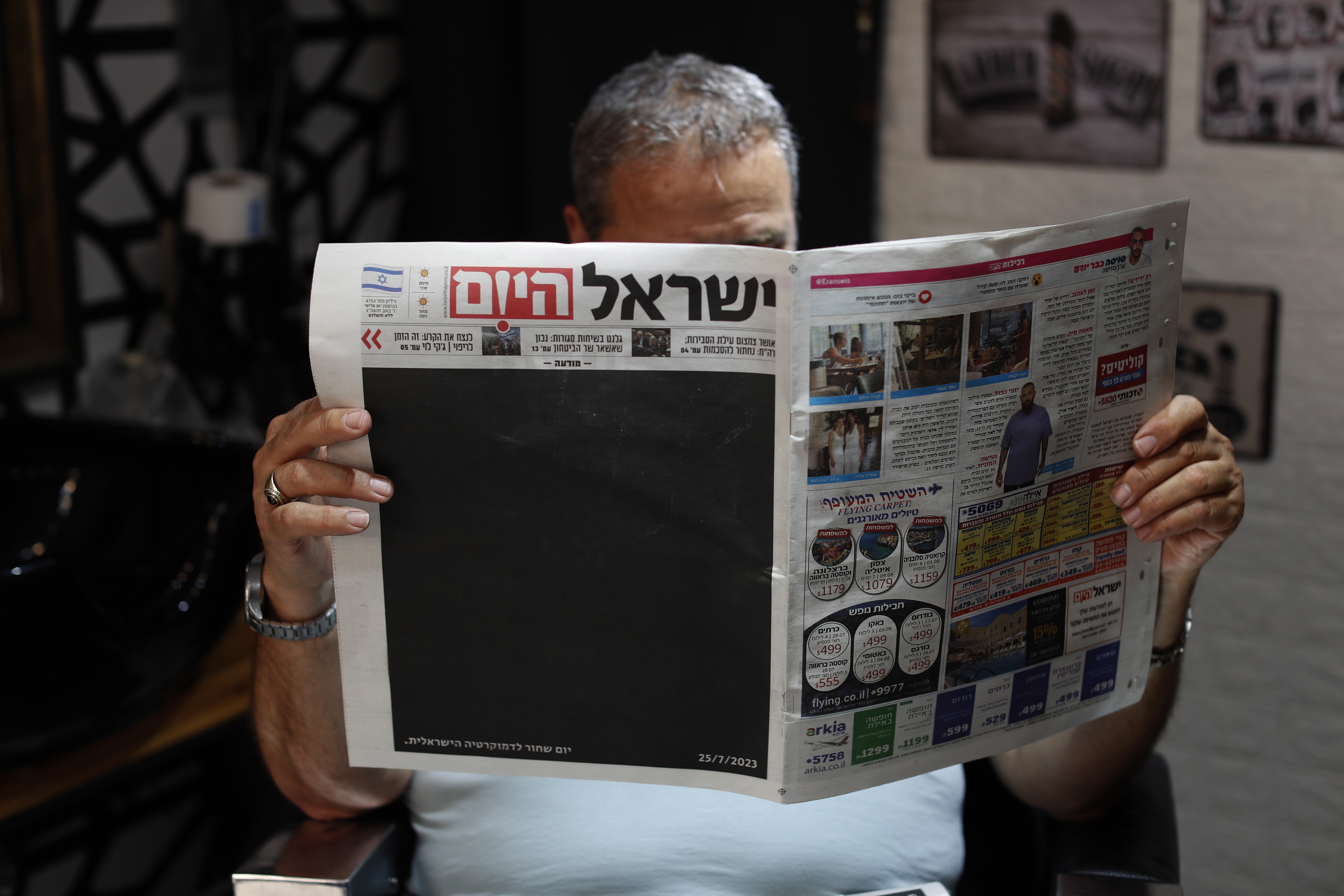 (Israel), 25/07/2023.- An Israeli hairdresser holds a copy of 'Israel Hayom' (Israel Today) newspaper with blacked out front page and headline reading in Hebrew 'Black Day for Israeli Democracy', in Jerusalem, 25 July 2023, one day after the Israeli parliament, or Knesset, passed a bill that would limit the Supreme Court's powers. (Protestas, Jerusalén) EFE/EPA/ATEF SAFADI