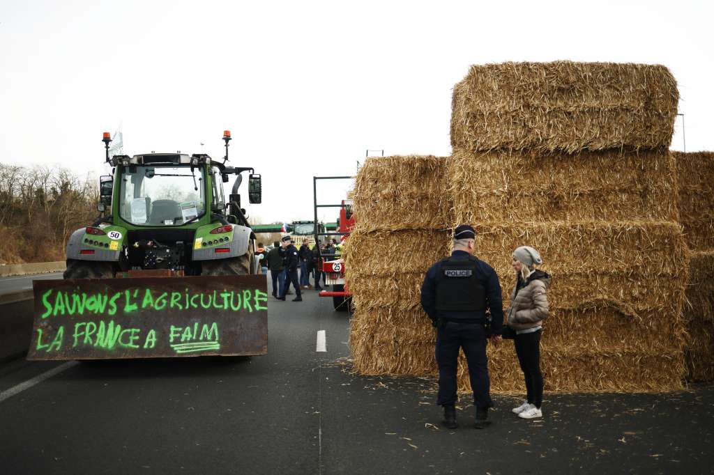Argenteuil (France), 29/01/2024.- A police officer talks to a farmer near a pile of hay next to a tractor with the message 'Save agriculture, France is hungry' during the blockade of the A15 motorway at Argenteuil, north of Paris, France, 29 January 2024. French farmers continue their protests with road blockades and demonstrations in front of state buildings awaiting a response from the government to their request for 'immediate' aid of several hundred million euros. On 23 January, the EU Agriculture and Fisheries Council highlighted the importance of providing the conditions necessary to enable EU farmers to ensure food security sustainably and profitably, as well as ensuring a fair income for farmers. (Protestas, Francia) EFE/EPA/YOAN VALAT