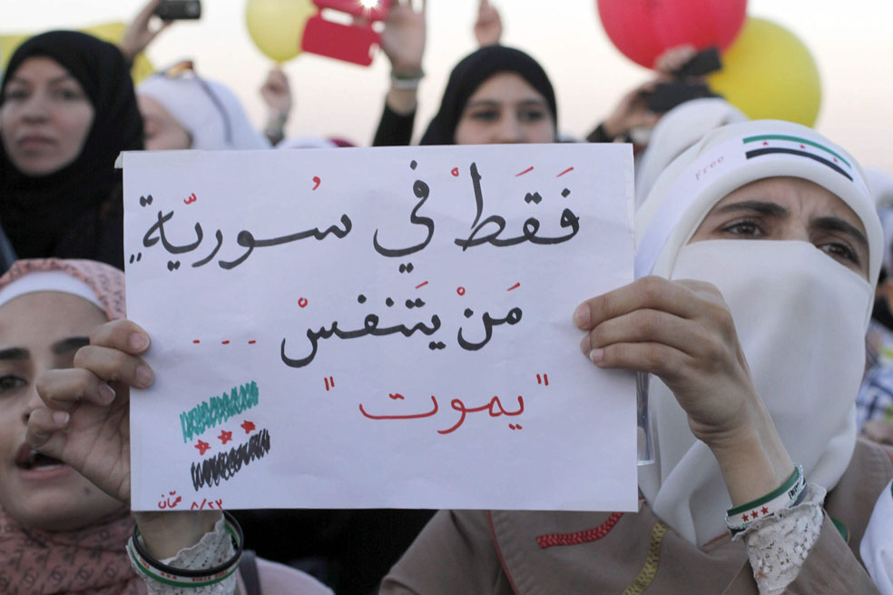 Un grupo de personas sirias muestra un cartel en árabe que dice "sólo en Siria, quien respira muere", y gritan eslóganes contra el régimen sirio frente a la Embajada siria en Ammán, Jordania. /EFE